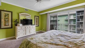 Ein Schlafzimmer mit Bett, Kommode, Fernseher und einem Balkon mit Geländer.