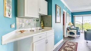 Een moderne keuken met witte kasten, een betegelde spatwand en uitzicht op een balkon met een blauwe bank.
