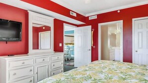 Een slaapkamer met een bed, een dressoir, een televisie en een deur naar een andere kamer.