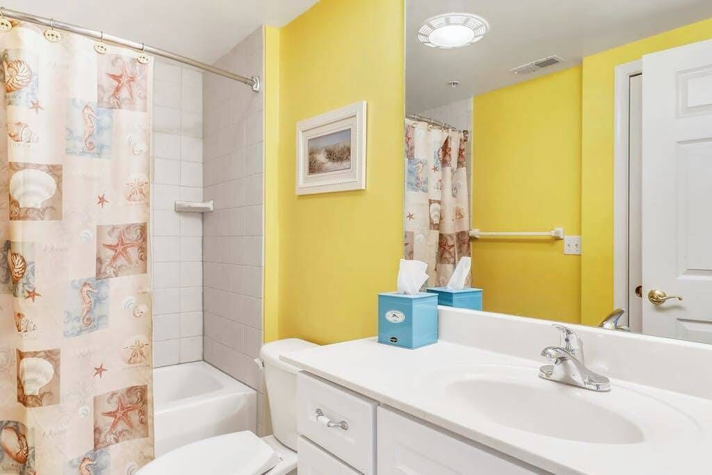 A bathroom with a shower curtain, a sink, a mirror, and a framed picture on the wall.