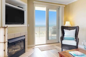 Ein Zimmer mit Kamin, Fernseher, Korbsessel und Blick auf den Strand durch eine Schiebetür.