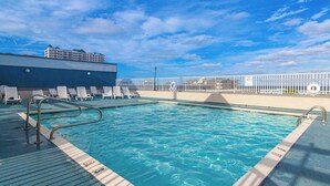 A swimming pool with lounge chairs, a white fence, and a building in the background. - Astoria 204 (Ocean City)
