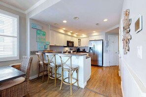 A kitchen with white cabinets, a stainless steel refrigerator, and a central island with bar stools. - Adagio 303 (Ocean City)