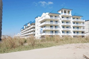 A beachfront hotel with multiple balconies, a clear sky, and a sandy beach in the foreground. - Adagio 303 (Ocean City)