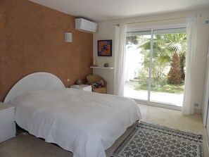 A bedroom with a bed, a chair, a small table, a shelf with decorative items, and a view of greenery through a sliding door. - St Cyprien Zen and Bohemian, a swimming pool just for you (Saint-Cyprien)
