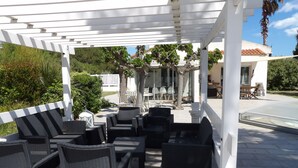En uteplats med möbler i rotting, en pergola och utsikt över ett hus och grönområden.