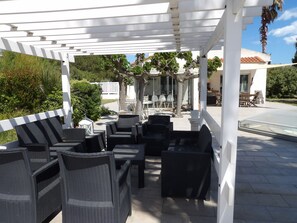 Eine Terrass mit Korbmöbeln, einer Pergola und Blick auf ein Haus und Grünflächen.