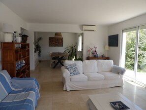Ein Wohnzimmer mit Sofa, Couchtisch, Bücherregal, Esstisch mit Stühlen und einem Bild an der Wand.
