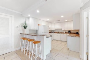 A modern kitchen with white cabinets, a granite countertop, and a central island with bar stools. - 4100 #102 (Ocean City)