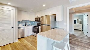 A modern kitchen with white cabinetry, stainless steel appliances, and a marble countertop. - 4100 #103 (Ocean City)