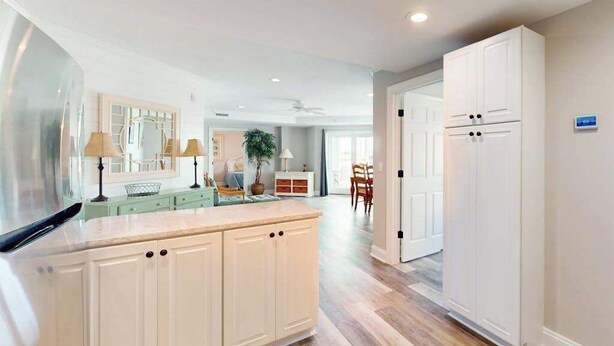 A modern kitchen with white cabinetry, a central island, and a dining area with a table and chairs. - 4100 #103 (Ocean City)