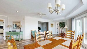 A dining room with a wooden table, chairs, a chandelier, and a view of the kitchen. - 4100 #103 (Ocean City)