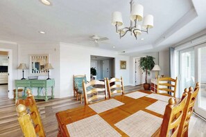 A dining room with a wooden table, chairs, a chandelier, and a view of the kitchen. - 4100 #103 (Ocean City)