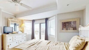 A hotel room with a bed, a television on a dresser, a window with curtains, and a ceiling fan. - 4100 #103 (Ocean City)