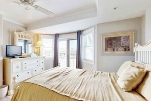 A hotel room with a bed, a television on a dresser, a window with curtains, and a ceiling fan. - 4100 #103 (Ocean City)