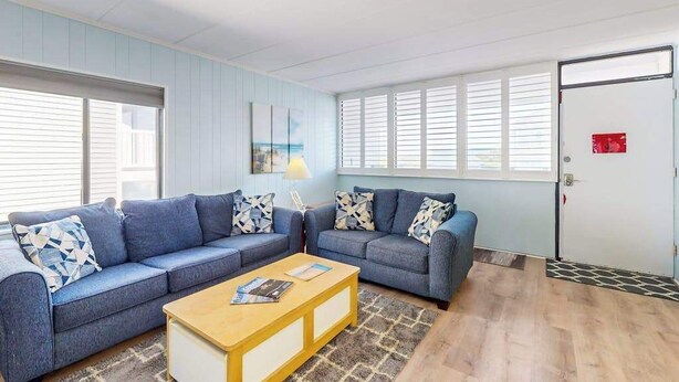 Ein Zimmer mit zwei Sofas, einem Couchtisch, einer Lampe und einer Tür mit einem roten Schild.