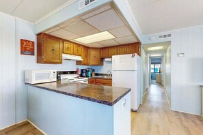 A kitchen with wooden cabinets, a granite countertop, a microwave, and a refrigerator. - Top-floor condo with balcony, walk 1 minute to the beach (Ocean City)
