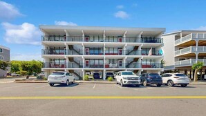 Ein mehrstöckiges Hotel mit Balkonen, einem Parkplatz und blauem Himmel.