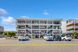 A multi-story hotel with balconies, a parking lot, and a clear blue sky. - Top-floor condo with balcony, walk 1 minute to the beach (Ocean City)