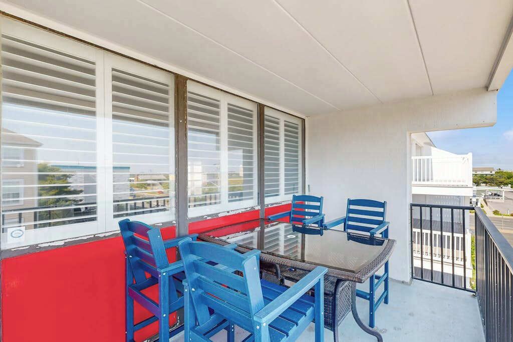 Een balkon met een tafel en stoelen, grote ramen met zonwering en uitzicht op de omgeving.