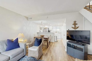 A modern living room with a sofa, a TV, a dining area, and a kitchen in the background. - Beach Club 109 B (Ocean City)
