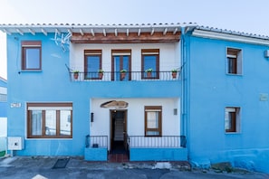 A two-story building with a balcony, a wooden door, and potted plants.