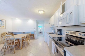A modern kitchen with white cabinets, a dining table with chairs, and a built-in oven. - Casa Serena (Ocean City)