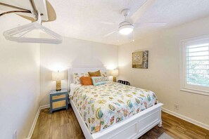 A bedroom with a bed, bedside tables, a ceiling fan, a window, and a wall clock. - Updated condo with balcony, washer/dryer & beach access - near dining & golf (Ocean City)
