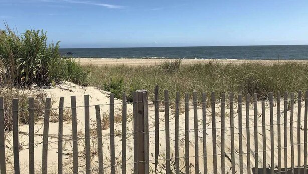 A beach with a wooden fence in the foreground and a clear sky.