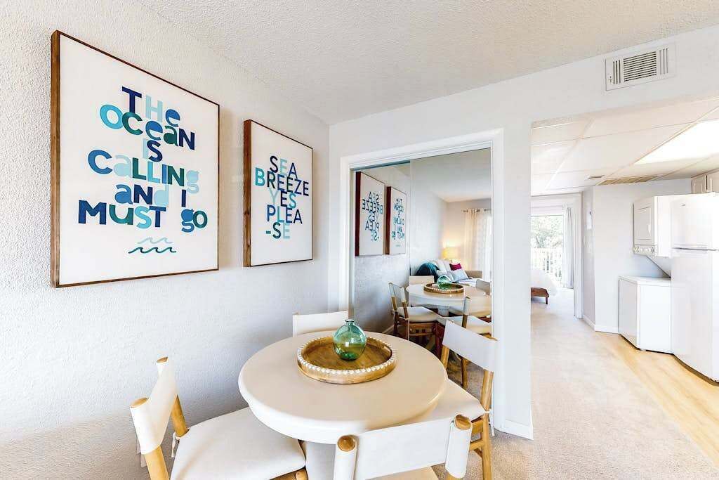 Ein modernes Interieur mit Essbereich, der einen runden Tisch und Stühle beinhaltet, einer Küchenzeile mit weißen Schränken und Kunstwerken an den Wänden.