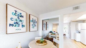 A modern interior with a dining area featuring a round table and chairs, a kitchen area with white cabinetry, and artwork on the walls.