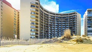 A high-rise hotel with multiple balconies, a sandy foreground, and a clear blue sky. - High Point South 6C (Ocean City)