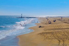 Ein Strand mit Menschen, einem Leuchtturm und blauem Himmel.