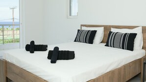 Una camera da letto con un letto in legno, biancheria da letto bianca, asciugamani neri e un condizionatore d'aria.