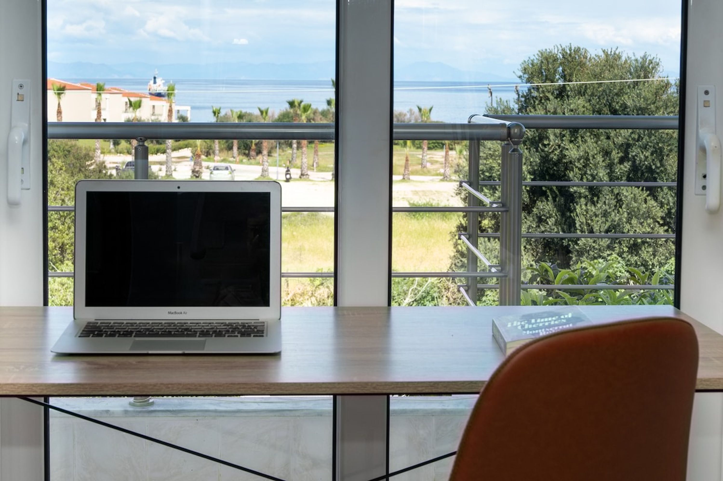 Un ordinateur portable est posé sur une table, avec vue sur un balcon et la mer.