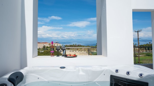 Una vasca idromassaggio con vista sull'oceano e un balcone con tavolo apparecchiato per due.