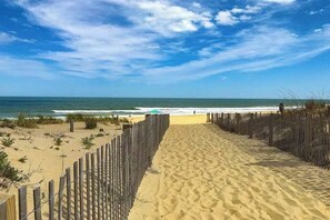 Uma trilha de areia que leva ao oceano, com uma cerca de madeira de um lado.