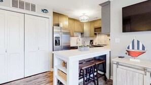 A kitchen with a central island, wooden cabinets, a refrigerator, and a decorative ship model. - Club Ocean Villa II 141 (Ocean City)