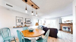 A dining area with a round wooden table, four teal chairs, and pendant lights.