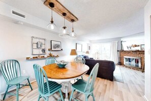 A dining area with a round wooden table, four teal chairs, and pendant lights. - Bermuda Bay 9 (Ocean City)