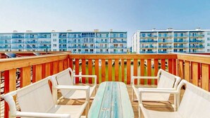 A rooftop deck with white chairs and a wooden table, overlooking a row of blue and white buildings.