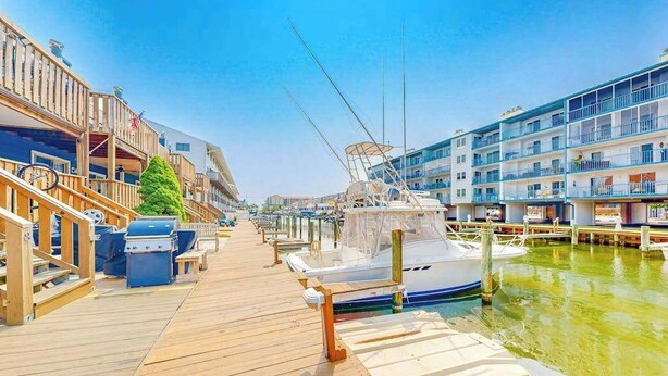 A marina with wooden walkways, boats docked, and multi-story buildings with balconies.