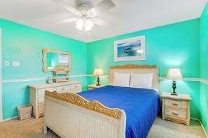 Ein Schlafzimmer mit einem Bett, Nachttischen, einem Deckenventilator, einem Spiegel und einem gerahmten Bild an der Wand.
