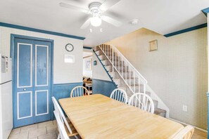 Ein Zimmer mit einem Holzespeisetisch, weißen Stühlen, einer blauen Tür, einer weißen Treppe und einem Deckenventilator.