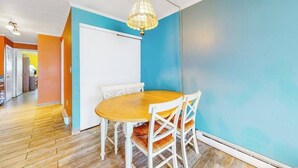 Uma sala de jantar com mesa redonda de madeira e cadeiras brancas, luminária pendente e parede azul.