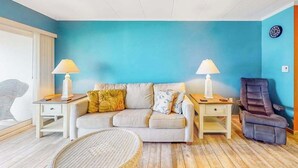 Uma sala de estar com parede azul, um sofá, duas mesas de cabeceira com abajures, uma poltrona reclinável e uma cadeira de vime.