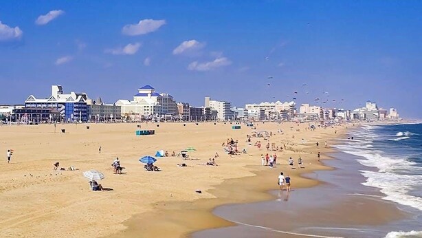 Uma praia com pessoas, guarda-sóis e edifícios ao fundo.