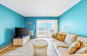 A living room with a TV, sofa, and wicker chair. - Oceanfront Condo with Beach Views, WiFi, Washer-Dryer, Parking & Walkable Locale (Ocean City)