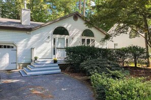 A single-story house with a garage, a front porch with steps, and a well-maintained lawn. - Tranquil Woods (Ocean Pines)