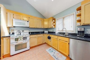 A kitchen with wooden cabinets, a microwave, stove, sink, and a coffee maker. - Tranquil Woods (Ocean Pines)